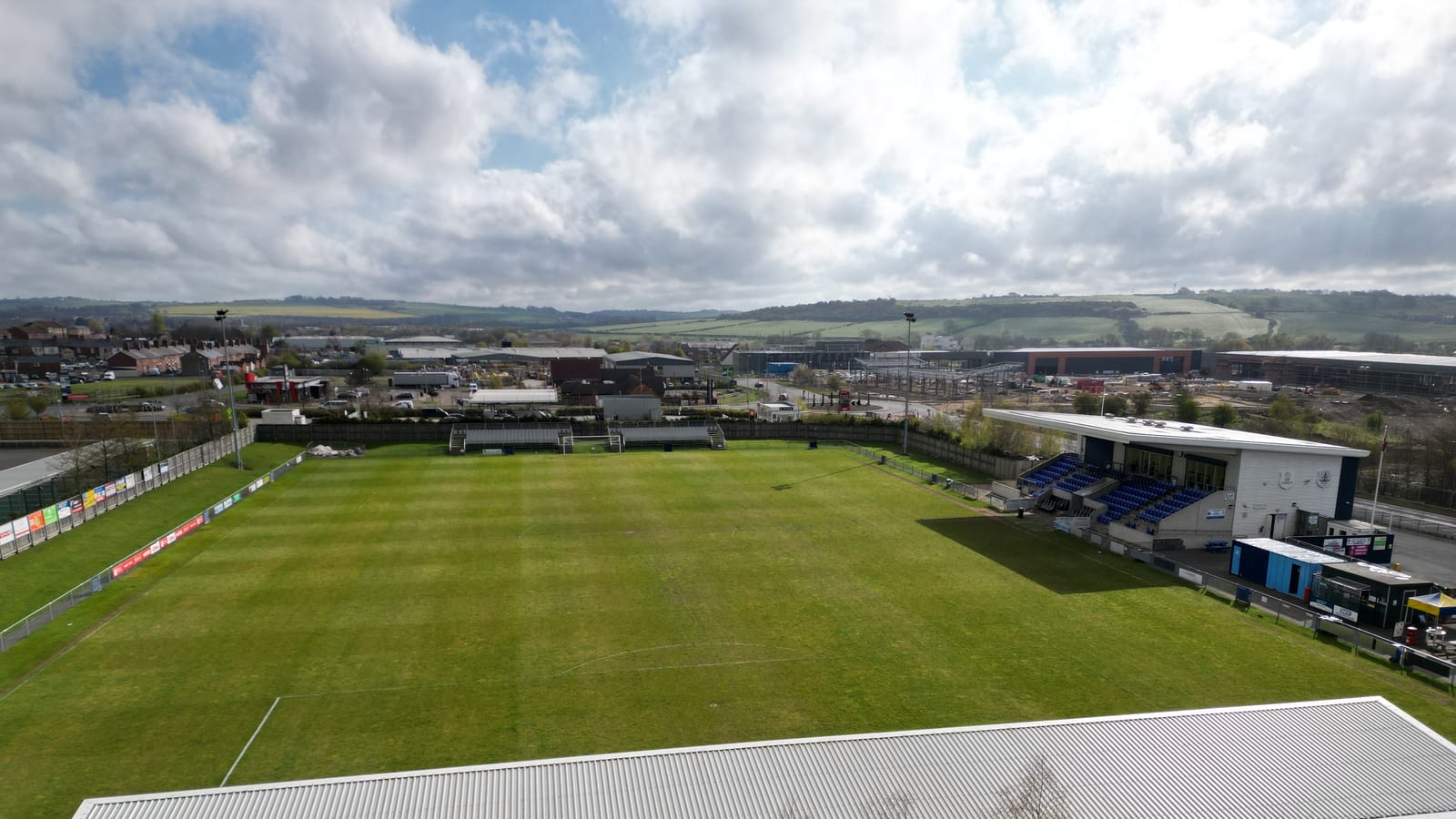 Aerial view over the Bishop Auckland Football Club pitch and grandstand, its solar-clad roof alongside