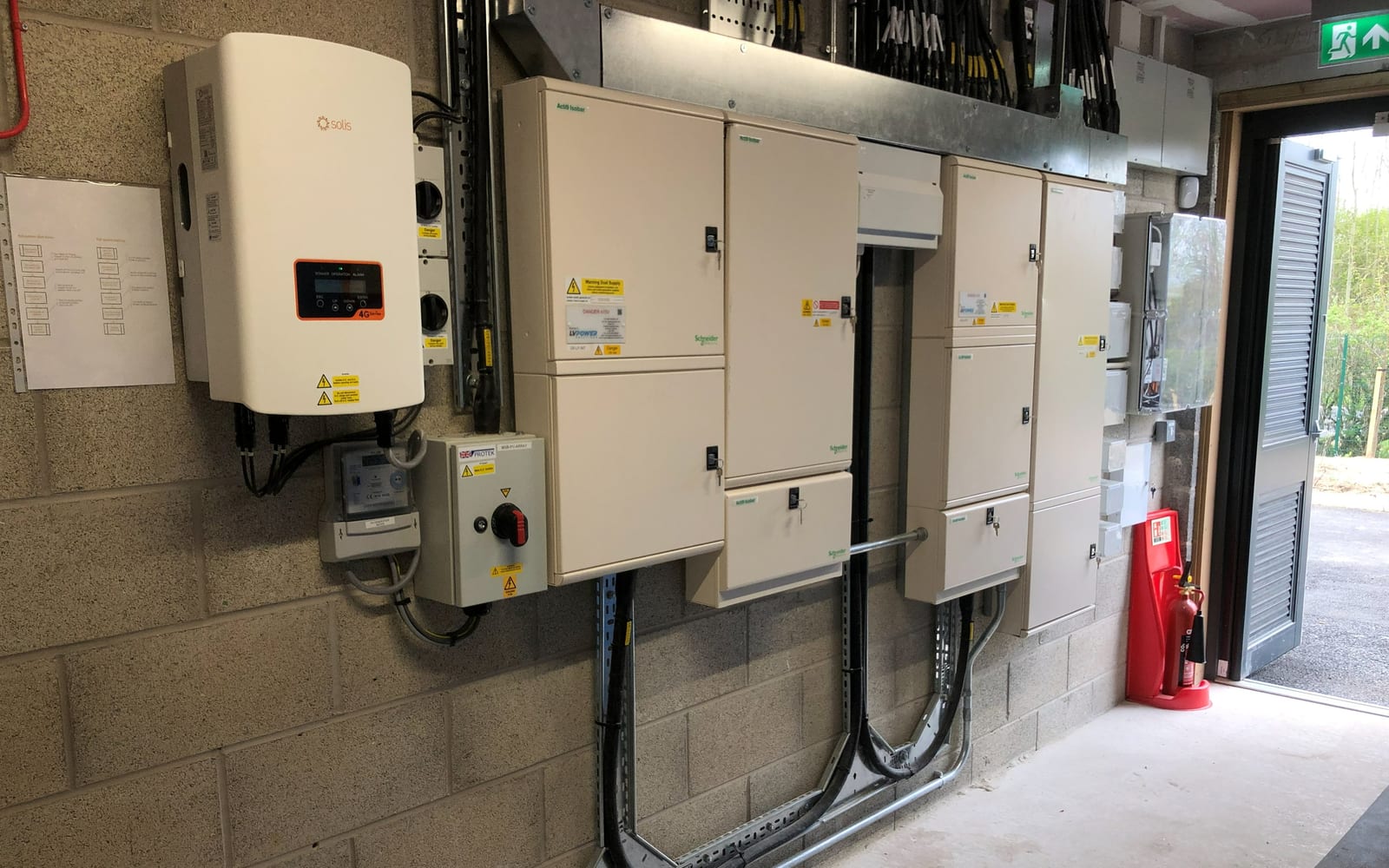Commercial solar inverters and isolators wired on a plant-room wall