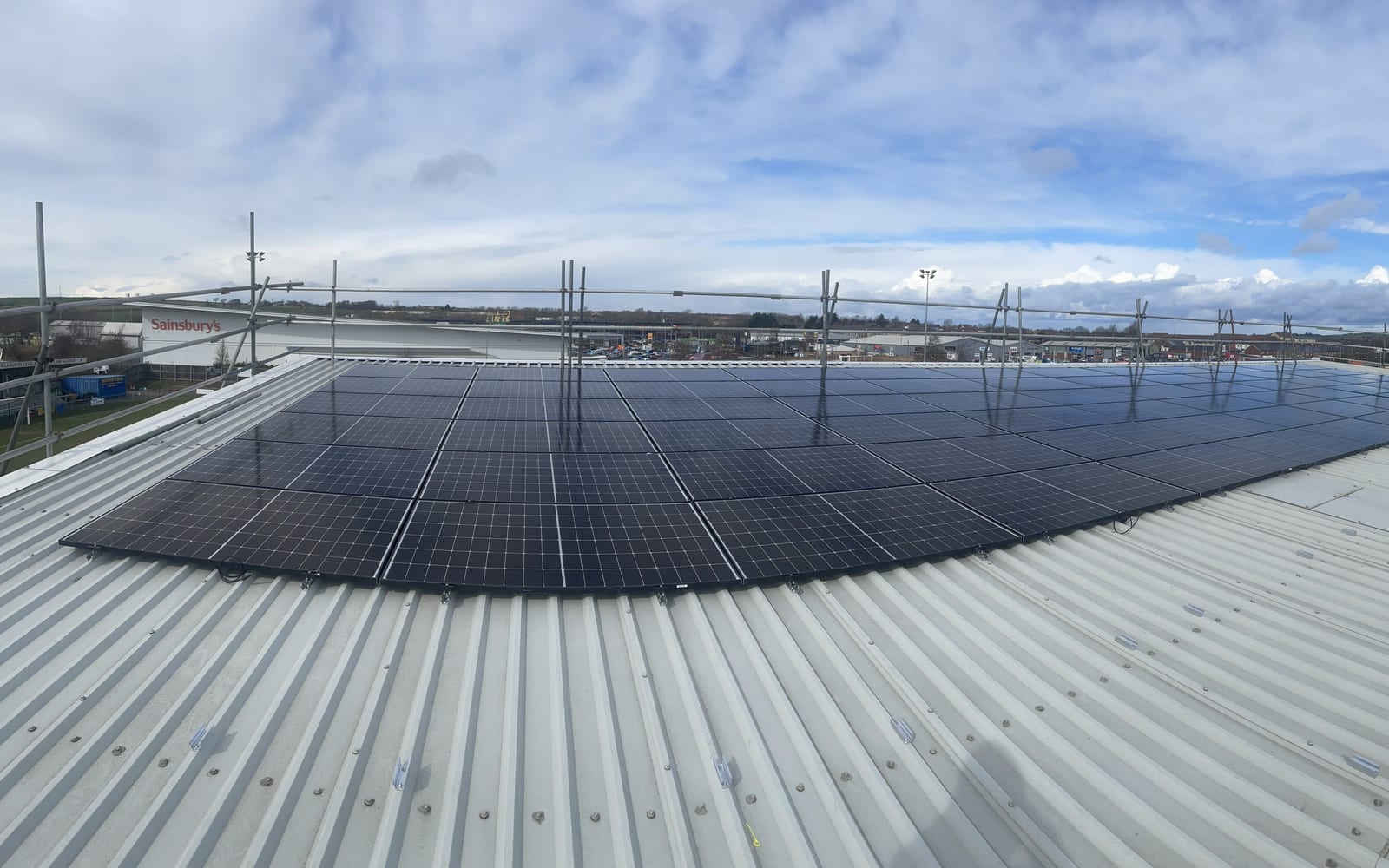 A completed commercial rooftop solar array in bright daylight, an estuary and bridge beyond
