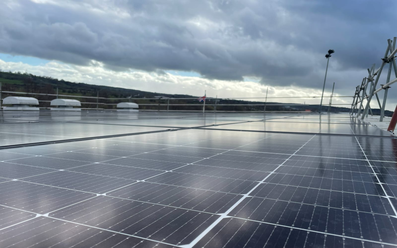 Low-angle view along a rooftop solar array with hills beyond